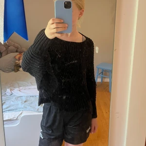 Svart oversized stickad tröja - Svart stickad tröja med oversized passform och breda, långa ärmar. Tröjan har ett grovt stickat mönster och är lite genomskinlig på vissa partier. Perfekt för lager-på-lager och chill stil.