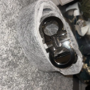 Svart Ferragamo skärp med metallspänne - Snyggt svart bälte från Ferragamo i äkta skinn med ikoniskt metallspänne i silverfärg. Bältet har en stilren och klassisk design med präglad storlek på insidan. Perfekt accessoar för att lyfta din outfit.