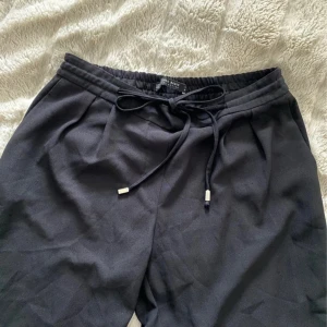 Svarta mjukisbyxor från Zara Basic - Svarta mjukisbyxor från Zara Basic med dragsko i midjan och resår. Byxorna har raka ben, diskreta bakfickor och är gjorda i ett mjukt, lätt material. Perfekta för en chill och stilren look.