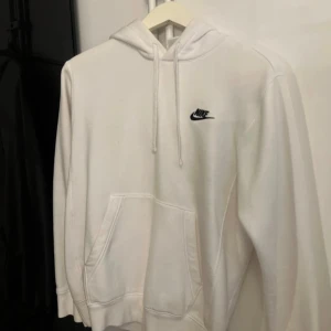 Vit Nike hoodie i strl XS - Snygg vit hoodie från Nike i storlek XS. Klassisk design med svart Nike-logga på bröstet, huva med snörning och stor känguruficka framtill. Mjuk och skön bomullsblandning. Använd ett fåtal ggr och har inga defekter. Pris går att diskutera vid snabb affär😊