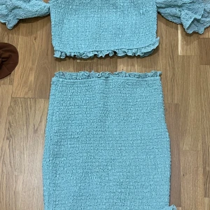 Ljusblå volangkjol i smock - Supersöt ljusblå kjol med smockat tyg och volangdetaljer upptill och nertill. Kjolen är kort och har en tight passform som framhäver figuren. Perfekt för dig som gillar en feminin och trendig stil.