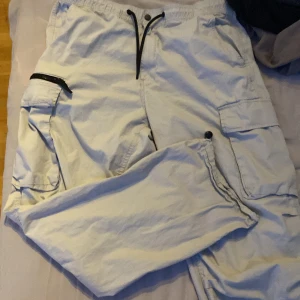 Ljusbeige cargopants med snörning - Säljer ett par ljusbeige cargopants med flera stora fickor på sidorna och en extra ficka med dragkedja. Byxorna har elastisk midja med svart snörning och är tillverkade i bomull. Perfekta för en chill och avslappnad stil.