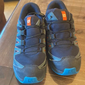 Salomon XA Pro 3D sneakers blå/orange - Salomon XA Pro 3D sneakers i mörkblå mesh med detaljer i blått och orange. Skorna har snabbsnörning, robust sula med grovt mönster för extra grepp och förstärkta partier i syntet. Perfekta för äventyr och utomhusaktiviteter.