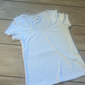 Vit spetskantad topp från Monki - Supersöt vit topp från Monki i storlek S med korta ärmar och rund halsringning dekorerad med spetskant. Tunt ribbat material. Inga defekter, bara använd ett fåtal gånger
