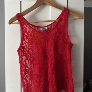 Röd spetslinne från Weekday XS - Säljer ett rött, transparent linne från Weekday i storlek XS. Toppen är helt i spets med blommigt mönster och har ärmlös design. Perfekt för att styla lager på lager eller för en statement-look.