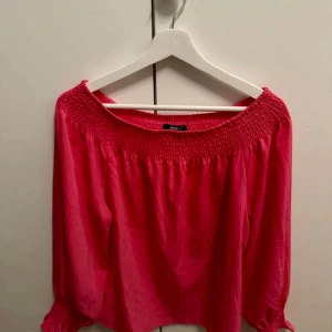 Rosa blus från Gina Tricot - Supersöt rosa blus från Gina Tricot med smockad resår upptill och vid ärmslut. Blusen har en lös passform och trekvartsärmar, perfekt för en fräsch och färgglad look. Tunn och luftig, passar perfekt till jeans eller kjol.