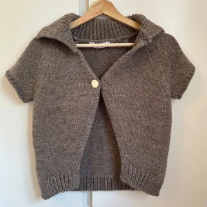 Brun stickad kofta från Zara - Kortärmad brun stickad kofta från Zara med bred krage och en stor knapp framtill. Koftan har ribbade muddar och en loose fit som ger en chill vibe. Perfekt att slänga över en t-shirt eller linne för en avslappnad look. Lånade bilder! Använd cirka 1-2 gånger 