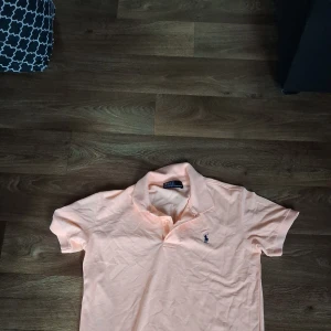 Ljusrosa pikétröja från Polo Ralph Lauren - Snygg ljusrosa pikétröja från Polo Ralph Lauren med klassisk krage och korta ärmar. Tröjan har det ikoniska broderade polospelar-loggan på bröstet och är gjord i mjuk bomull. Perfekt för en fräsch och stilren look.