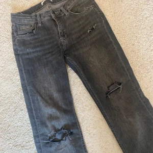 Grå slitna bootcut jeans - Säljer ett par supersnygga grå bootcut jeans med slitna detaljer och hål vid knäna. Dom har en liten slitning som kan bli ett hål men de kan lätt fixas!💘