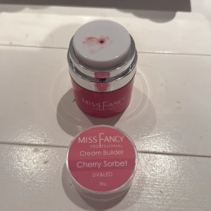 Miss Fancy Cream Builder Cherry Sorbet - Miss Fancy Professional Cream Builder i färgen Cherry Sorbet. En rosa krämig gelé för naglar, passar UV & LED-lampor. Kommer i en rund burk på 30g med silvriga detaljer och skruvlock. Perfekt för att bygga snygga och hållbara naglar med en fräsch rosa ton. Den är bara använd till ett sett 🥰