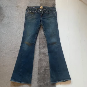 Blå bootcut jeans från True Religion - Snygga blå bootcut jeans från True Religion med klassisk femficksdesign och knappar på bakfickorna. Jeansen har en lätt slitning, de är vintage 