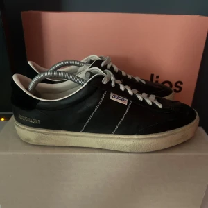 Svarta sneakers från Golden Goose - Snygga svarta sneakers från Golden Goose med vit sula och grå snörning. Skorna har en klassisk design med rund tå och märkets logga på sidan. Perfekta för en stilren look. Skorna är knappast använda och köpta ifrån care of carl . Tveka inte på att fråga om skorna . Säljer pga för stora 