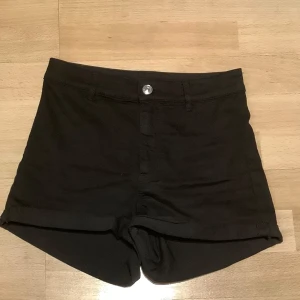Svarta shorts från Divided - Snygga svarta shorts från Divided med knapp och dragkedja framtill. De har en klassisk design med uppvikta ben och två bakfickor. Perfekta för en stilren look. Använda en gång.