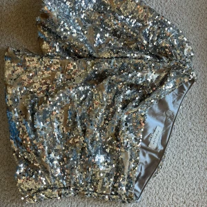 Glittrig paljetttopp från By Malina - Snygg och glittrig one shoulder top täckt med silverfärgade paljetter. Perfekt för att lysa upp vilken kväll som helst. Toppen har lite av en kortare längd men en bekväm passform. Lite puffärm! Använd 1 gång och nypris är ca 2200kr✨🤍🩶 strlk e xs men passar S! 
