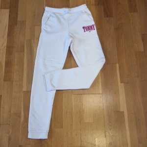 Vita mjukisbyxor från Tommy Hilfiger - Säljer ett par vita mjukisbyxor från Tommy Hilfiger med broderad logga i rosa. Byxorna har en bekväm passform med resår i midjan och muddar vid bensluten. Perfekta för en avslappnad stil.