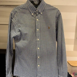 Blårutig skjorta från Ralph Lauren - Snygg blårutig skjorta från Ralph Lauren i slim fit. Skjortan har långa ärmar och knappar framtill samt en broderad logotyp på bröstet. Perfekt för en stilren look.