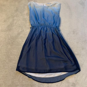 Blå ombreklänning - Snygg ärmlös klänning i blå ombre med elastisk midja och rund hals. Perfekt för sommarens alla tillfällen. Den har en lätt och luftig känsla med en något längre baksida.