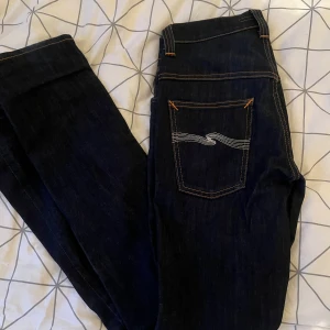 Mörkblå jeans från Nudie Jeans - Snygga mörkblå jeans från Nudie Jeans med klassisk femficksdesign och kontrastsömmar. Byxorna har en normal passform och är tillverkade i högkvalitativt denim. Perfekta för en stilren look.Pris kan diskuteras 
