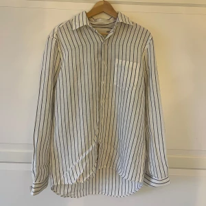 Vit och blå randig skjorta från A Day's March - Säljer en stilren vit skjorta med blå ränder från A Day's March. Skjortan har långa ärmar och en klassisk krage. Perfekt för en avslappnad men ändå uppklädd look. Den är tillverkad i ett lätt och bekvämt material. Vid frågor & funderingar är det bara att höra av dig! 