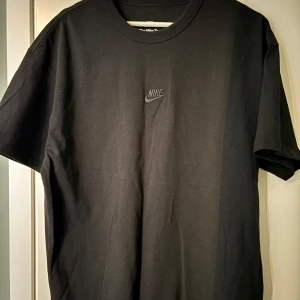 Svart t-shirt från Nike - Säljer en svart t-shirt från Nike med deras klassiska logga på bröstet. T-shirten har en loose fit och är tillverkad i mjukt bomullsmaterial. Perfekt för en avslappnad stil.