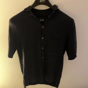 Mörkblå kortärmad kofta från only & sons - Snygg mörkblå kortärmad tröja från only & sons med korta ärmar och knappar framtill. Den har en praktisk bröstficka och en klassisk krage. Perfekt för en stilren look till sommaren.