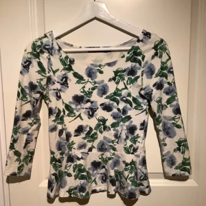 Blommig topp från BikBok - Säljer en söt blommig topp från BikBok i storlek XS. Toppen har ett vackert blommönster i grönt och blått med vitt. Den har trekvartsärmar och en lätt utsvängd nederdel som ger en fin siluett. Perfekt för vårens och sommarens dagar!