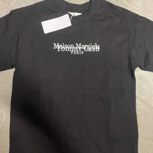 Svart t-shirt från Maison Margiela - Snygg svart t-shirt från Maison Margiela med tryck i vitt på framsidan och ett unikt nummermönster på baksidan. Perfekt för dig som vill ha något stilrent men ändå iögonfallande. Tommy cash X maison margiella t shirt. Helt ny. Skriv till mig vid mer frågor eller för mer bilder🤩💫