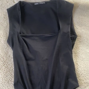 Svart ärmlös bodysuit från Zara - Snygg svart ärmlös bodysuit från Zara med en stilren design. Perfekt för att matcha med olika outfits. Materialet är mjukt och stretchigt för en bekväm passform.