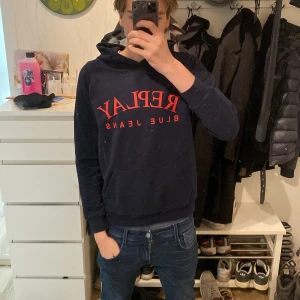 Mörkblå hoodie från Replay - Säljer en mörkblå hoodie från Replay med röd text 'Replay Blue Jeans' på framsidan. Säljer hoodien för att den e för kort. Skriv om ni har frågor!!