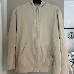 Beige huvtröja från Studio Total - Säljer en stilren beige huvtröja från Studio Total storlek M. Tröjan har dragkedja framtill och en huva. Perfekt för en avslappnad look. 