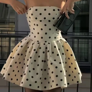 Prickig axelbandslös klänning - Snygg axelbandslös klänning i vitt med svarta prickar. Den har en kort och utsvängd kjol som ger en lekfull look. Perfekt för en somrig dag eller en festlig kväll. Klänningen har en söt rosett i ryggen som en extra detalj.