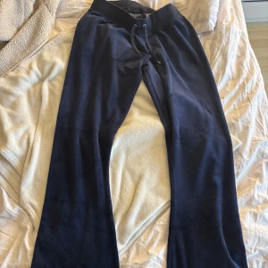 Mörkblå mjukisbyxor från Juicy Couture - Säljer ett par mörkblå mjukisbyxor från Juicy Couture. Byxorna har en bekväm passform med snörning i midjan och är tillverkade i ett mjukt material. Perfekta för en avslappnad stil. 💞
