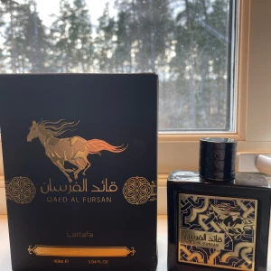 Qaed Al Fursan parfym från Lattafa - Elegant parfymflaska i svart med gyllene detaljer och ett hästmotiv på framsidan. Flaskan har en fyrkantig form och en stilren svart. korken är en svart magnetisk kork!  ⸻      Volym kvar: Cirka 75 ml (av totalt 90 ml)  Denna  parfym är en kraftfull och exotisk doft med tydlig ananaston i toppen, vilket ger en fruktig och frisk öppning. Under ananasen finns en varm bas av träiga och orientaliska noter som ger parfymen djup och långvarighet.