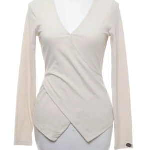 Beige omlottopp från Chiara Forthi - Säljer en stilren beige omlottopp från Chiara Forthi. Toppen har en v-ringad design och långa ärmar, perfekt för en elegant look. Materialet är ribbat vilket ger en fin struktur och passform. Storlek M