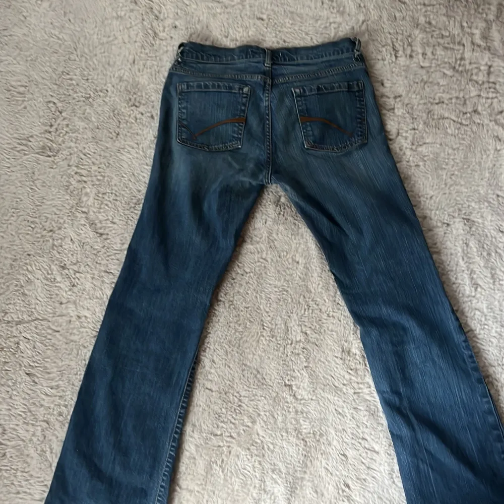 Säljer ett par klassiska blå jeans från Lindex. De har en blandning mellan rak och bootcut passform med femficksdesign och knappgylf. Perfekta för en avslappnad stil. Jeansen har tyvärr ett hål på båda sidorna som syns på sista bilden men går super enkelt att fixa med lite nål och tråd! Original priset ligger mellan 400-700kr.. Farkut & Housut.