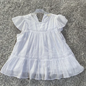 Vit blus från Gina Tricot  - Fin vit blus från Gina Tricot med volangdetaljer och korta ärmar. Perfekt för sommarens varma dagar. Blusen har en luftig passform och är tillverkad i ett lätt material.