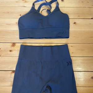 Mörkgrått träningsset  - Snyggt mörkgrått träningsset  med ribbad struktur med linne och shorts. Perfekt för träning med en bekväm passform och stilren design. Shortsen är högdmidjade och linnet har korsade axelband.