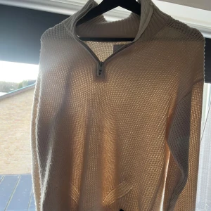Beige tröja med dragkedja från Calvin Klein Jeans - Säljer en stilren beige tröja från Calvin Klein Jeans. Tröjan har en dragkedja framtill och är tillverkad i ett stickat material som ger en skön och avslappnad känsla. Perfekt för kyligare dagar.