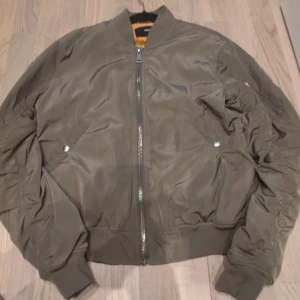 Olivgrön bomberjacka från BikBok - Snygg olivgrön bomberjacka från BikBok i storlek S. Jackan har en dragkedja framtill och ribbade muddar vid ärmslut och nederkant. Perfekt för en cool och avslappnad stil.