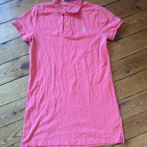Rosa pikéklänning från Ralph Lauren - Säljer en snygg rosa pikéklänning från Ralph Lauren med korta ärmar och klassisk krage. Klänningen har en liten broderad logga på bröstet och knappar framtill. Perfekt för en avslappnad stil med en touch av elegans. Hör av dig vid intresse!💕
