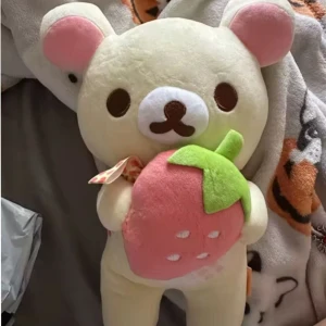 Rilakkumma, Korilakumma björn med jordgubbe, Gosedjur, plush, ny - Söt rilakkumma / korilakumma nallebjörn i ljusgul färg med rosa öron och en stor rosa jordgubbe med gröna blad. Den har ett prickigt band runt halsen. Perfekt för att kramas med eller som dekoration i rummet. Mått ca 27cm hög.