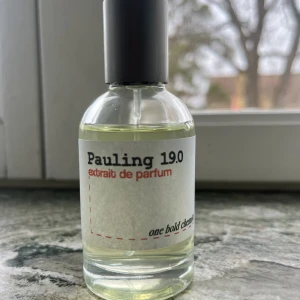 Pauling 19.0 extrait de parfum - Säljer en flaska Pauling 19.0 extrait de parfum. Flaskan är genomskinlig med en enkel vit etikett och svart text. Parfymen har en stilren design med en svart kork. Perfekt för den som söker en unik doftupplevelse.