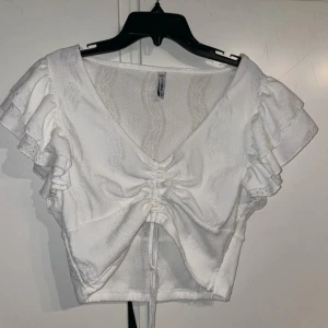 Vit blus från FB Sister - Säljer en söt vit blus från FB Sister med volangärmar och knytning framtill. Blusen har en v-ringad design och är croppad, perfekt för sommarens varma dagar.