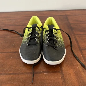 Svarta och gula sneakers med snörning - Snygga inneskor i svart och gult med snörning. Skorna har en cool design med en gradvis övergång från svart till gult och en vit sula. Perfekta för en sportig look.