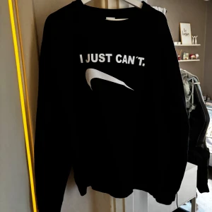 Svart sweatshirt från AWDis - Säljer en svart sweatshirt från AWDis med texten 'I JUST CAN'T.' på framsidan. Tröjan har långa ärmar och en klassisk rund halsringning. Perfekt för en avslappnad stil.
