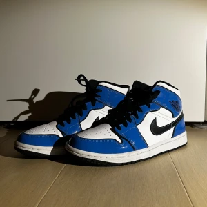Nike Air Jordans i blått och vitt - Snygga Nike Air Jordans i en fräsch blå och vit färgkombination med svarta detaljer. Skorna har klassisk snörning och den ikoniska Air Jordan-loggan på sidan. Perfekta för dig som vill ha en stilren och sportig look.