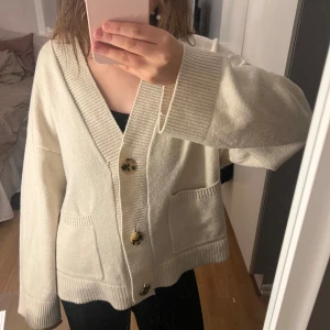 Vit kofta med knappar - Säljer en mysig vit kofta med stora knappar och två fickor framtill. 