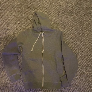 Grå hoodie från Pier One - Säljer en stilren grå hoodie från Pier One med dragkedja och justerbar huva. Perfekt för en avslappnad look. Den har långa ärmar och är gjord i ett mjukt material för extra komfort. Modellen är 180