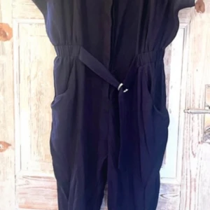 Svart jumpsuit med knytband - Snygg marinblå jumpsuit med knytband i midjan för en justerbar passform. Den har korta ärmar och praktiska fickor på sidorna. Perfekt för en stilren look.