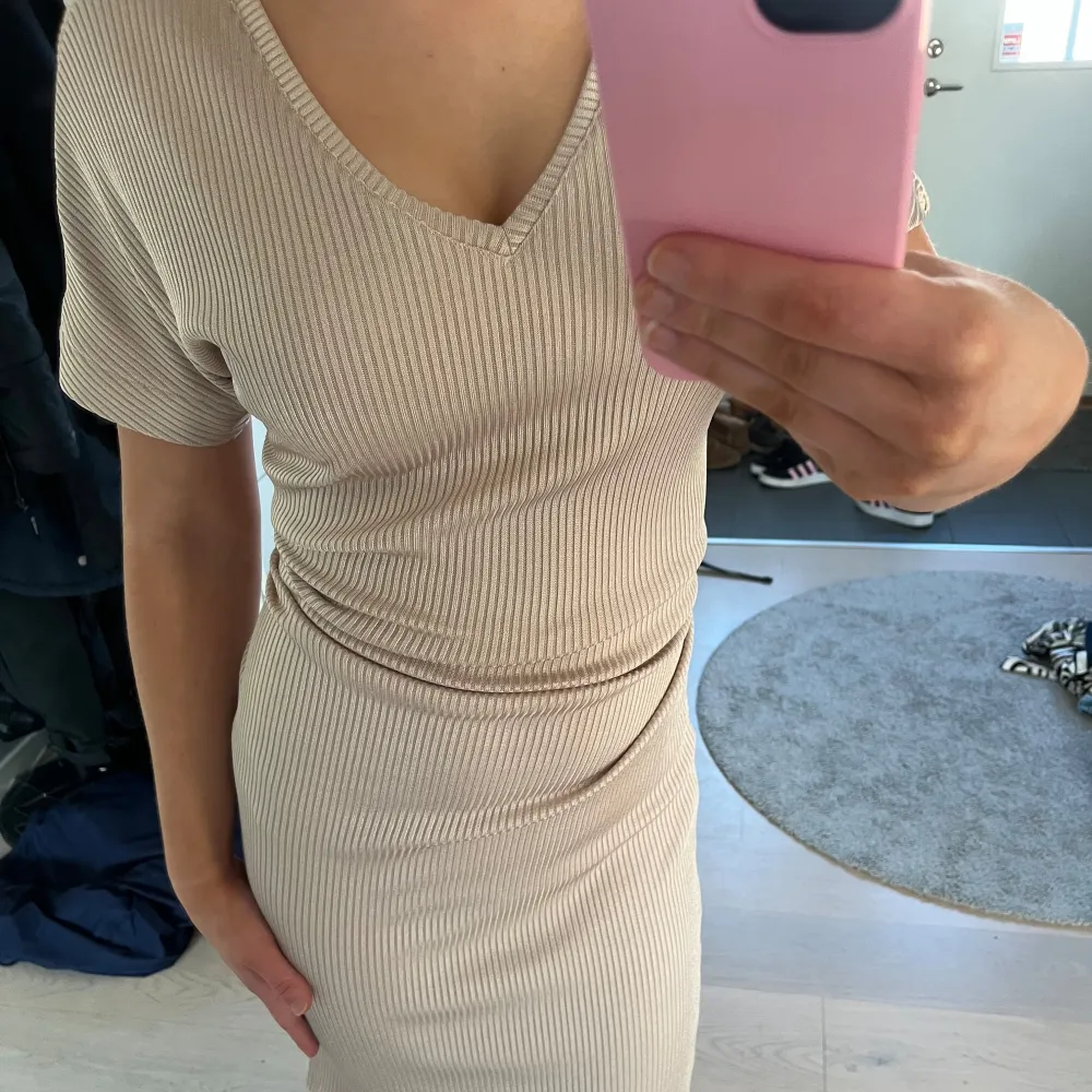 Säljer en snygg beige ribbad klänning med v-ringning och korta ärmar. Klänningen har en tight passform som framhäver figuren. Perfekt för en stilren look. Klänningen är i storlek xs från Lindex . Mekot.